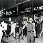 Policeman watches demonstrators sporting posters of Lt. Gilligan and demanding justice.