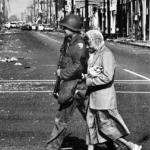 
A cause for civility - A Guardsmen walks an elderly woman across the shattered intersection of Wilmington and the riot scarred 103rd Street.. 