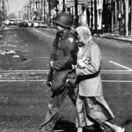 A cause for civility - A Guardsmen walks an elderly woman across the shattered intersection of Wilmington and the riot scarred 103rd Street.. 